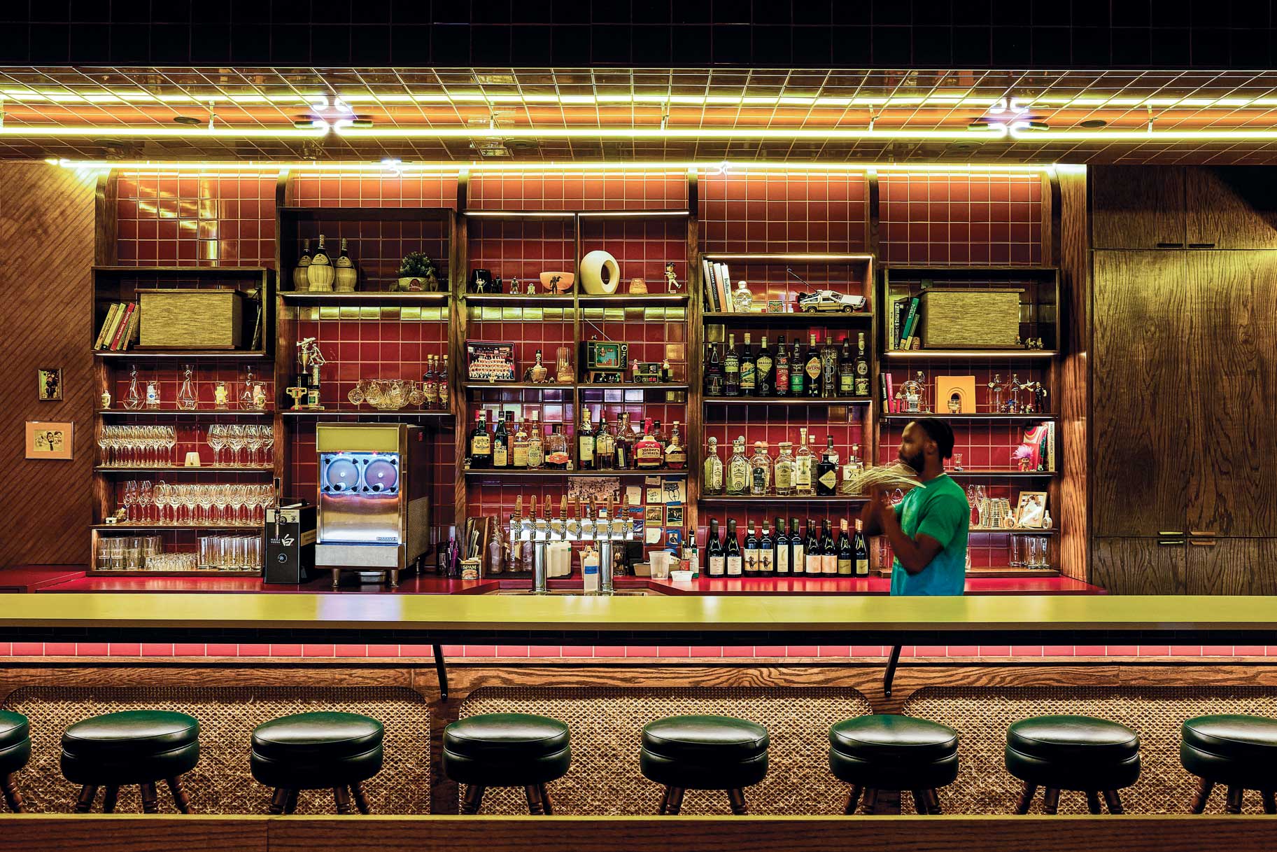 A bartender shakes a beverage behind a bar lined with alcohol containers.