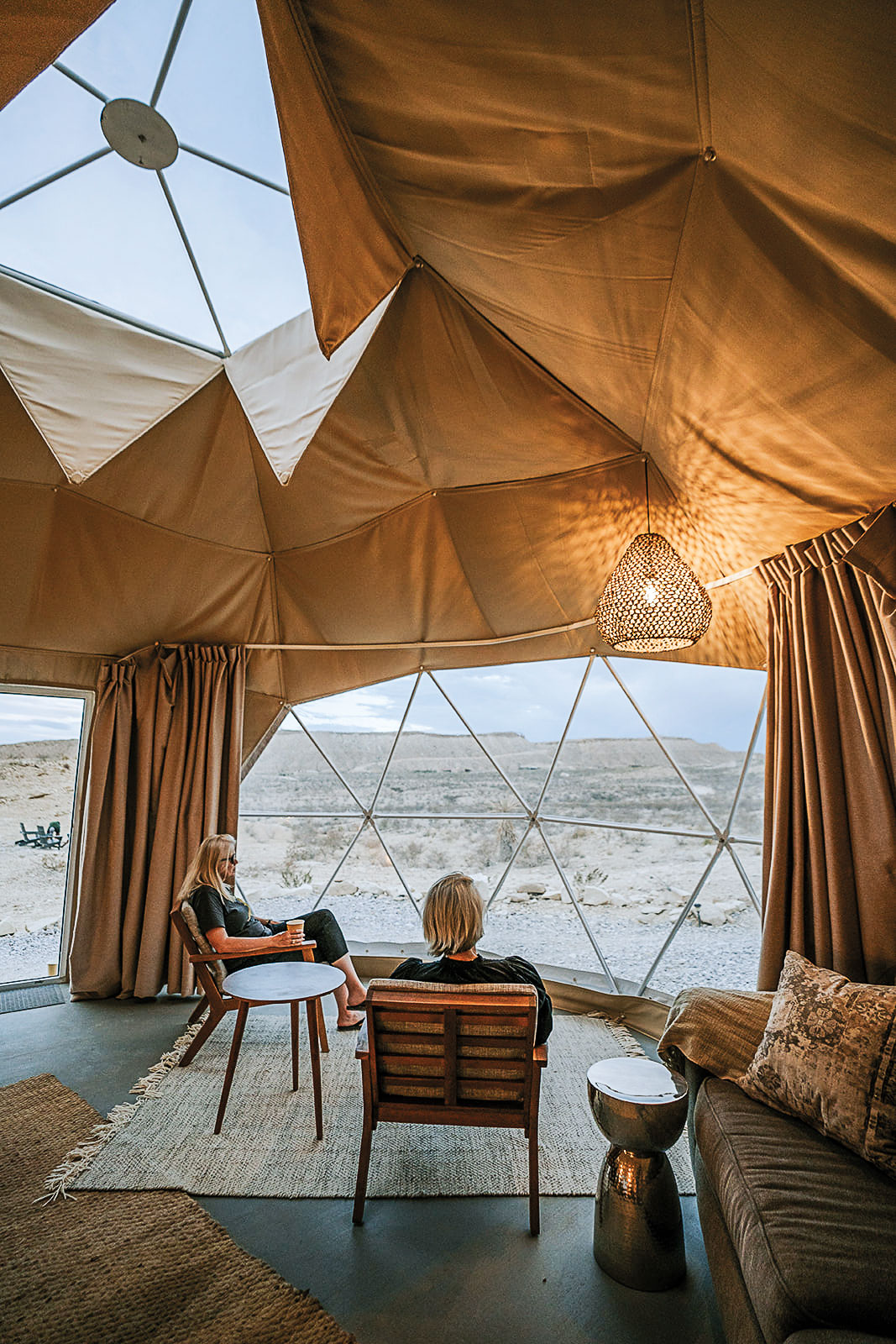 Two people sit in chairs staring at the desert through windows.