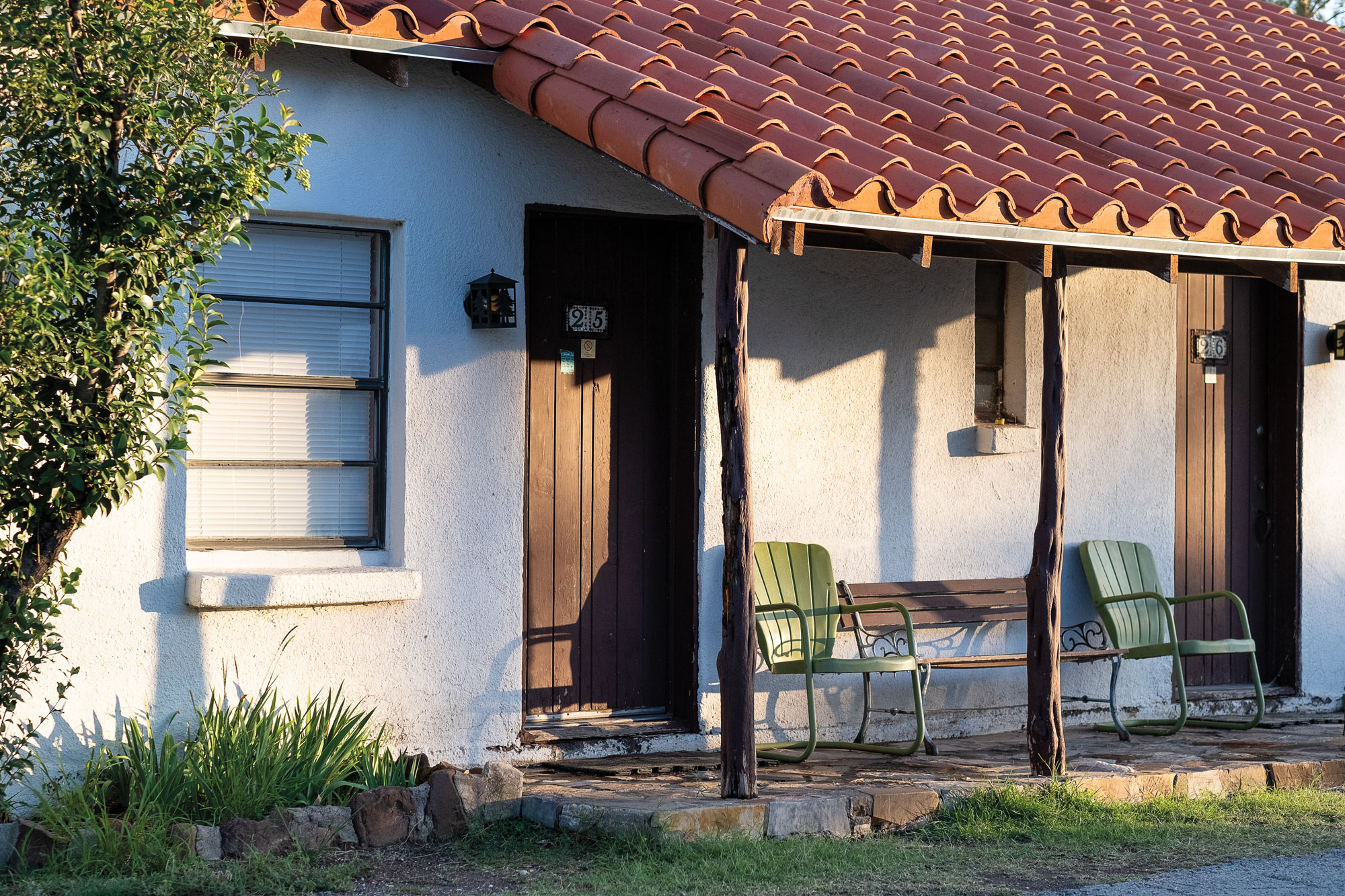 A white adobe building with a wooden porch and red shingled roof