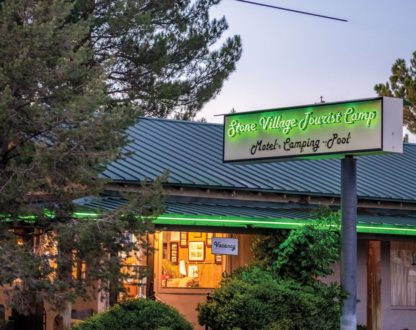 An illuminated building at dusk with a lit sign that reads "Stone Village Tourist Country" in a neon green.