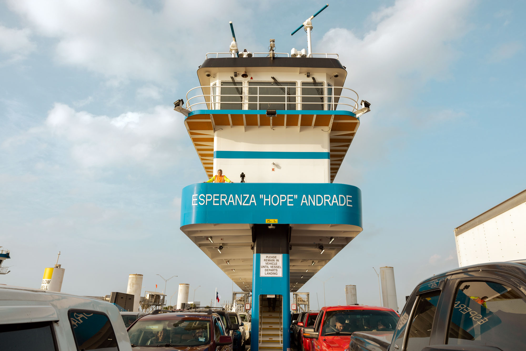 A large teal and white ferry carry multiple cars and passengers