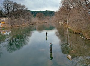 Two people fly-fishing in a river surrounded by bare trees