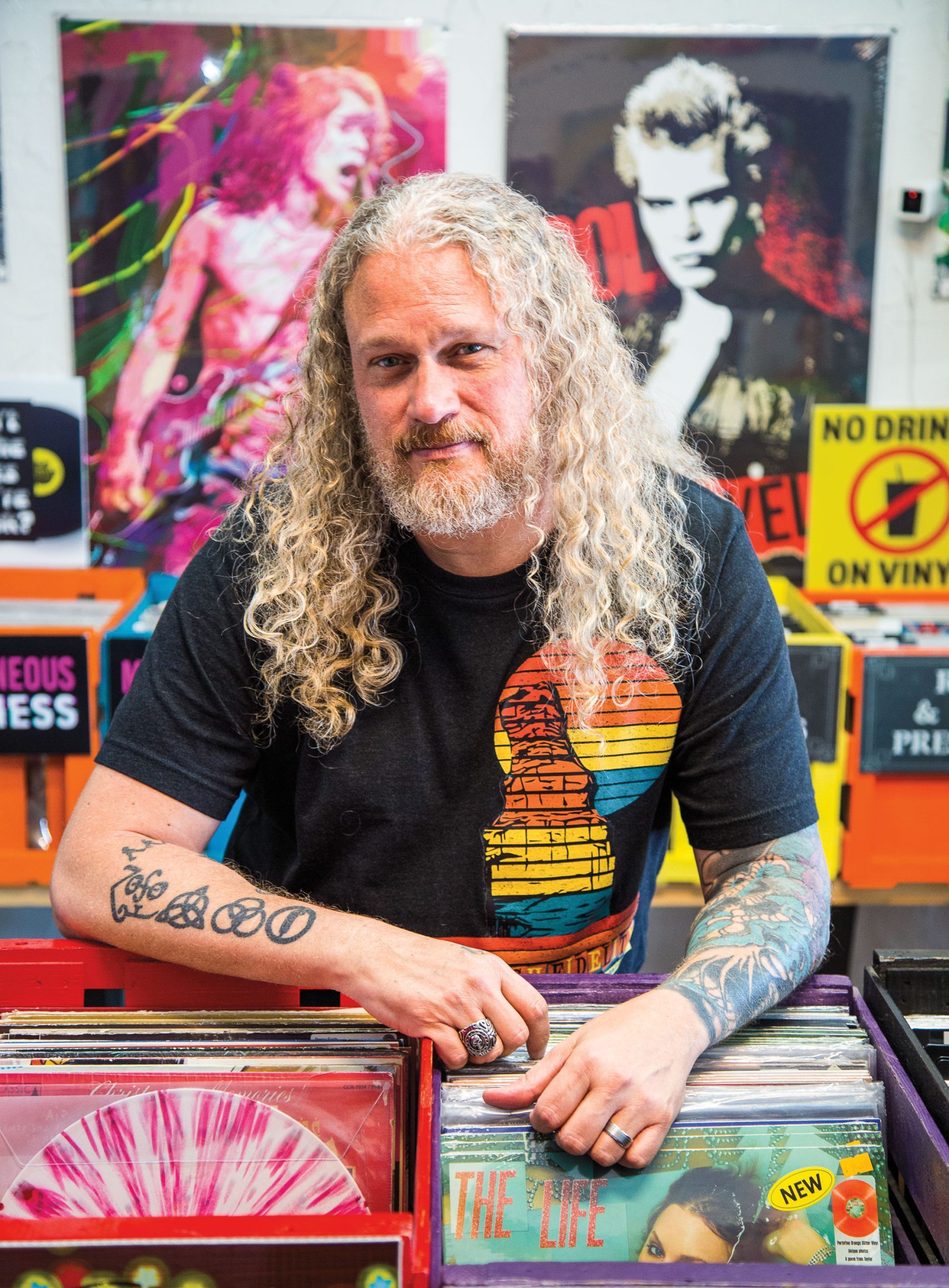 A man with long gray hair poses while resting on a rack of vinyl records