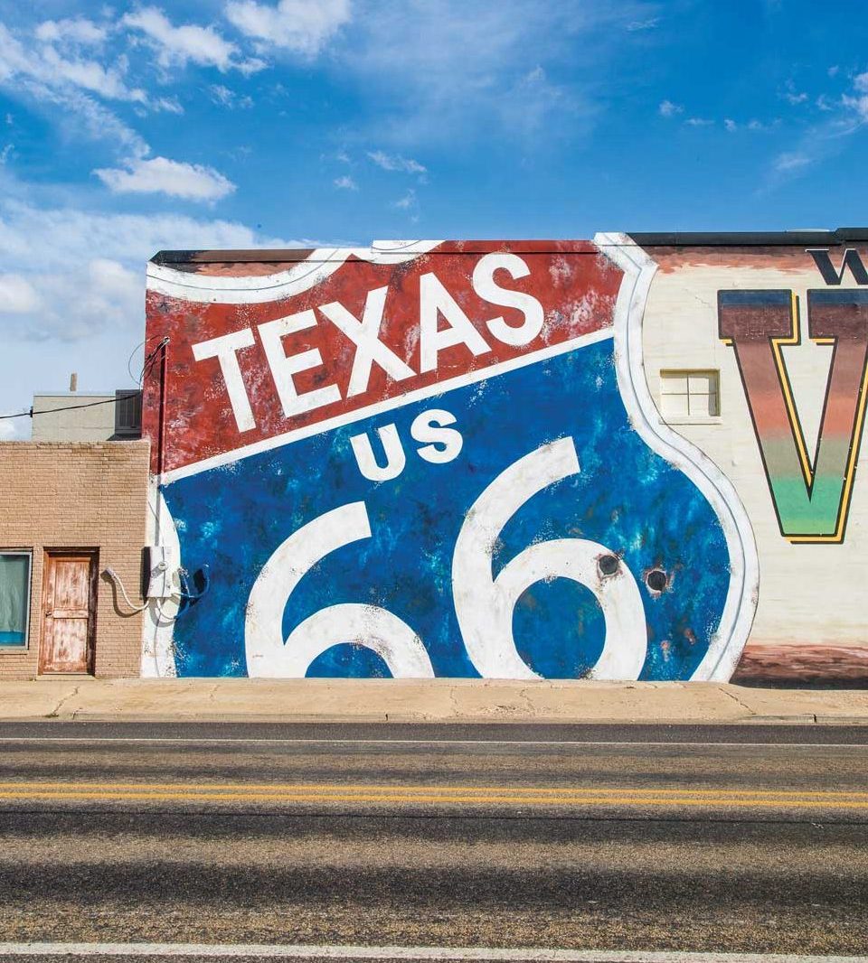 A mural on the side of a building featuring a road sign that reads "Texas US 66" in red, white, and blue.