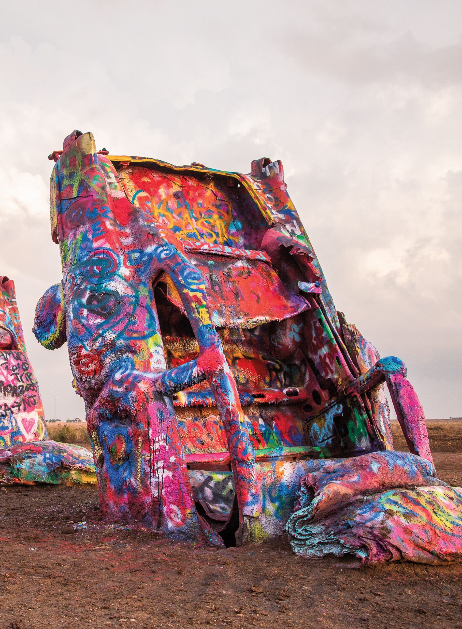 A retro car buried in the ground is covered in multicolor graffitti