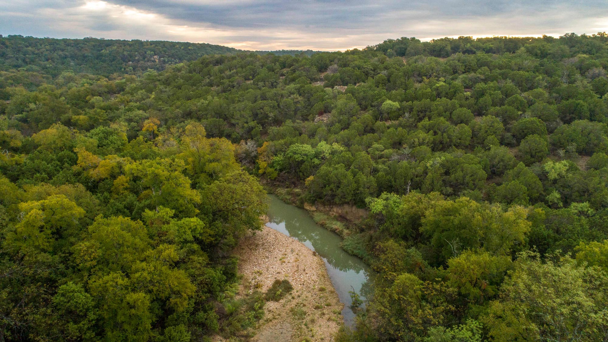 An aerial view of a river running through a sprawling tree-filled landscape