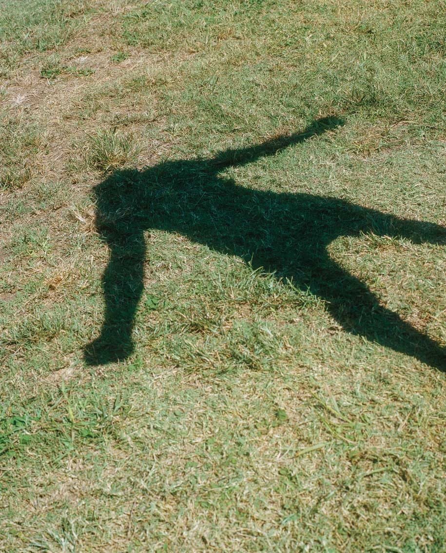 The shadow of a man holding his arms out to his sides cast on a grass lawn