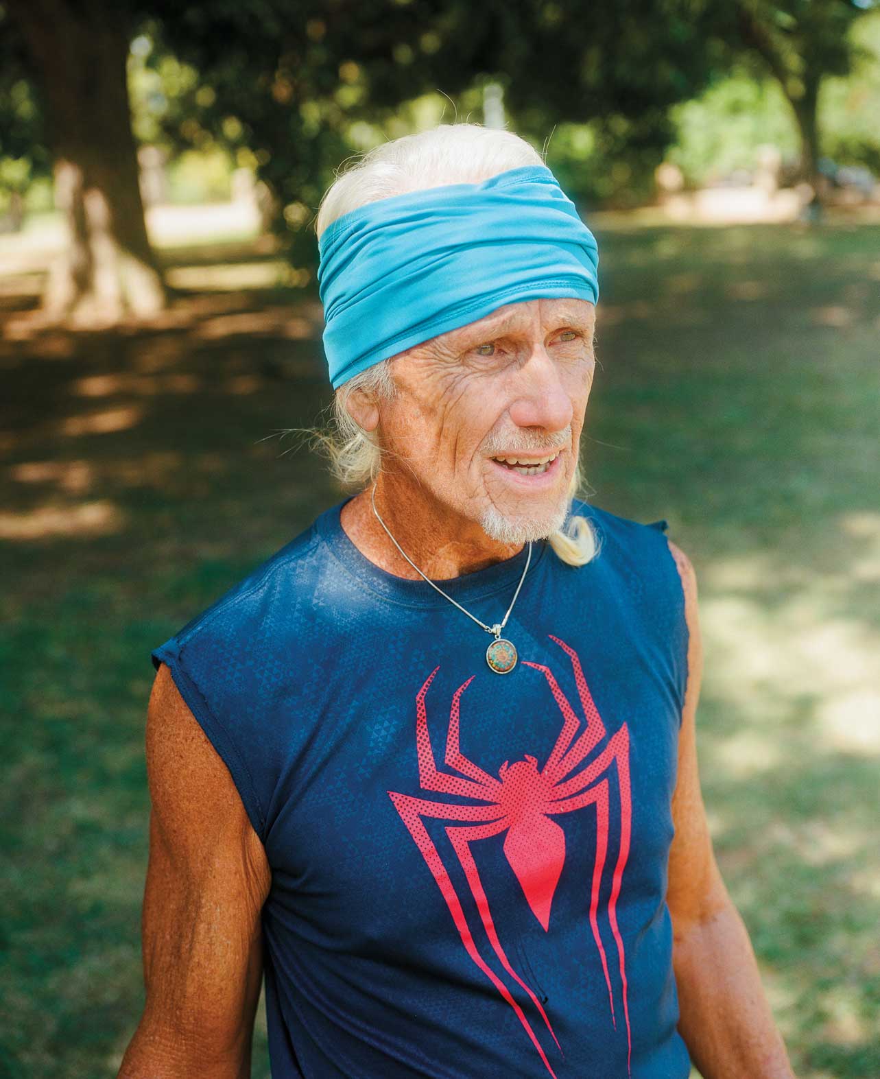 An older man in a blue bandana and a blue cut-off tank with a red spider print