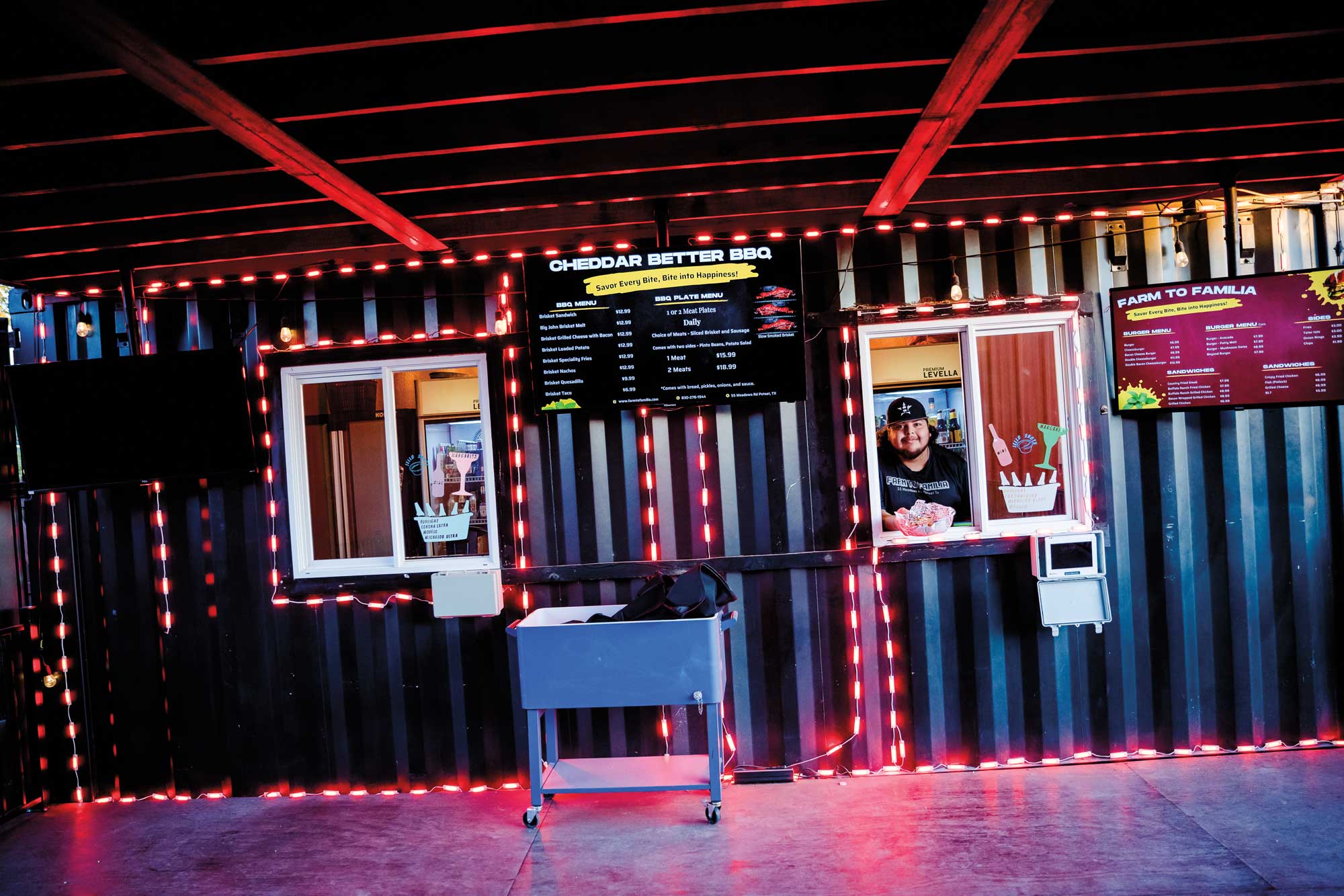 A person in a black hat and black shirt holding a basket of food in an ordering window in-between two wall-mounted menus