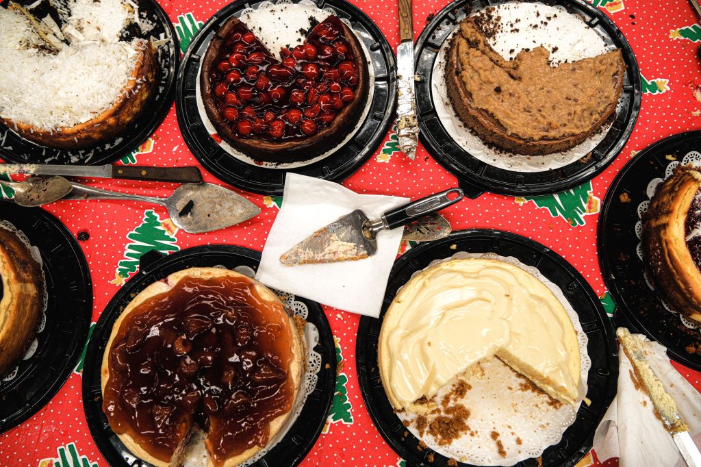 Seven cheesecakes on a red and green tablecloth with illustrations of Christmas trees