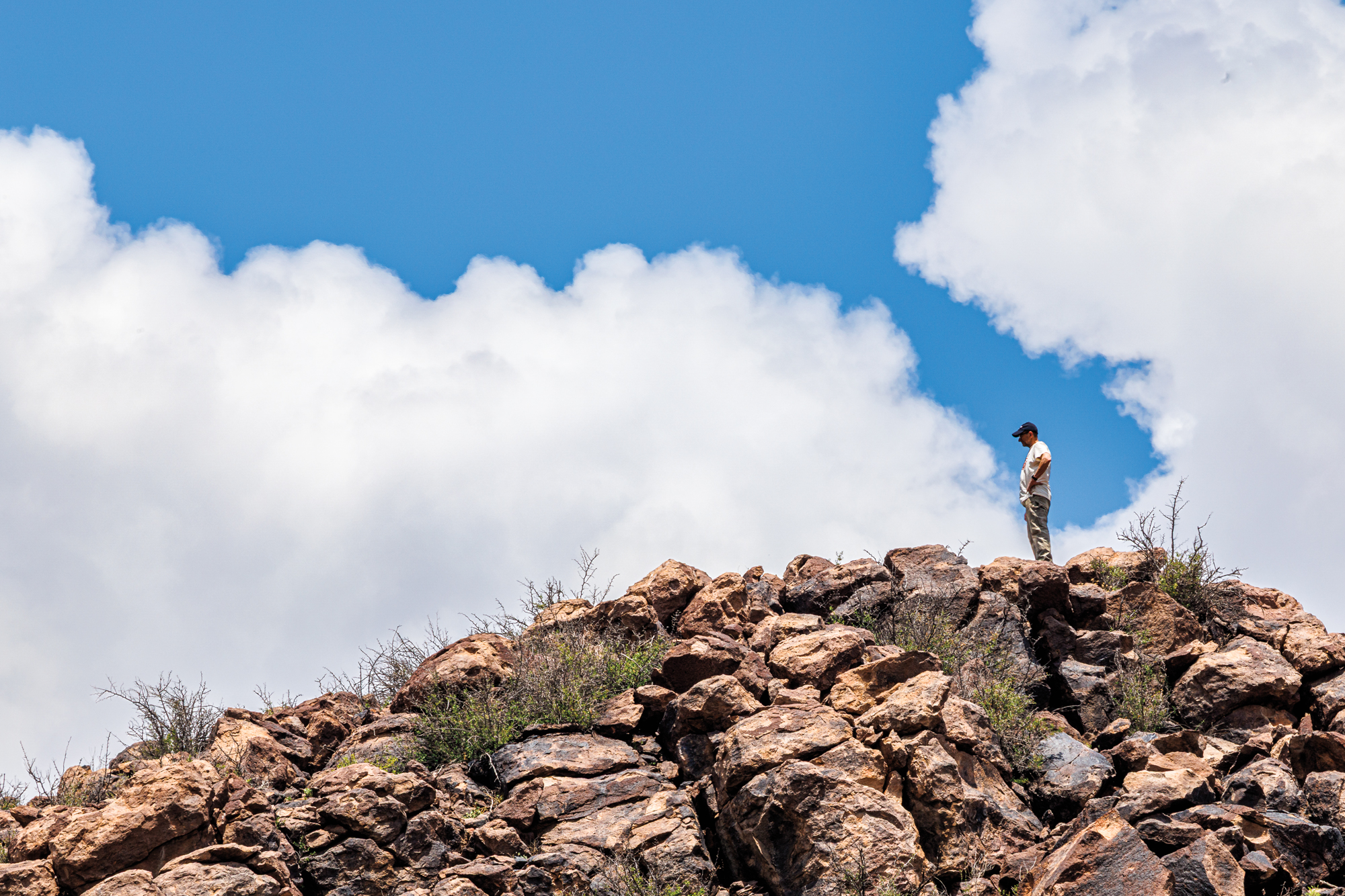 A man peers down from the top of a rocky slope