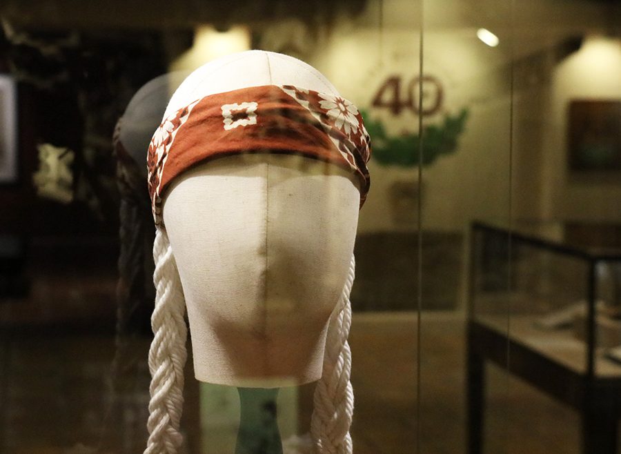 A mannequin head wearing a red bandana and long white braids in a museum display case