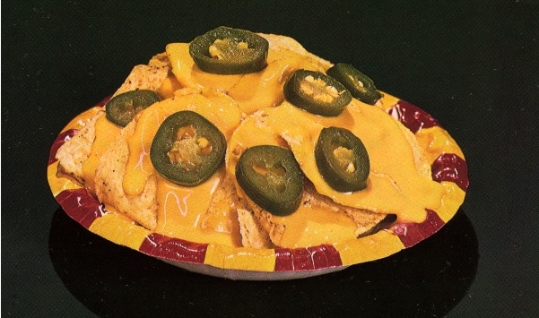 A red and yellow bowl filled with round tortilla chips covered in melted yellow cheese and sliced jalapenos