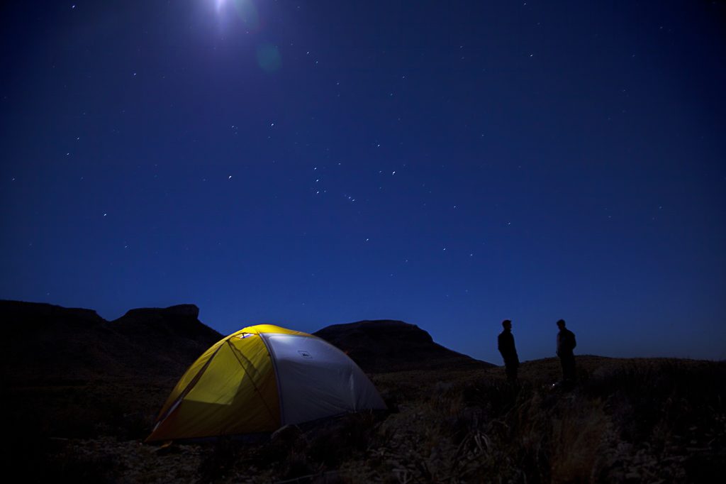 A yellow and white tent with two people standing next to it at night under the stars