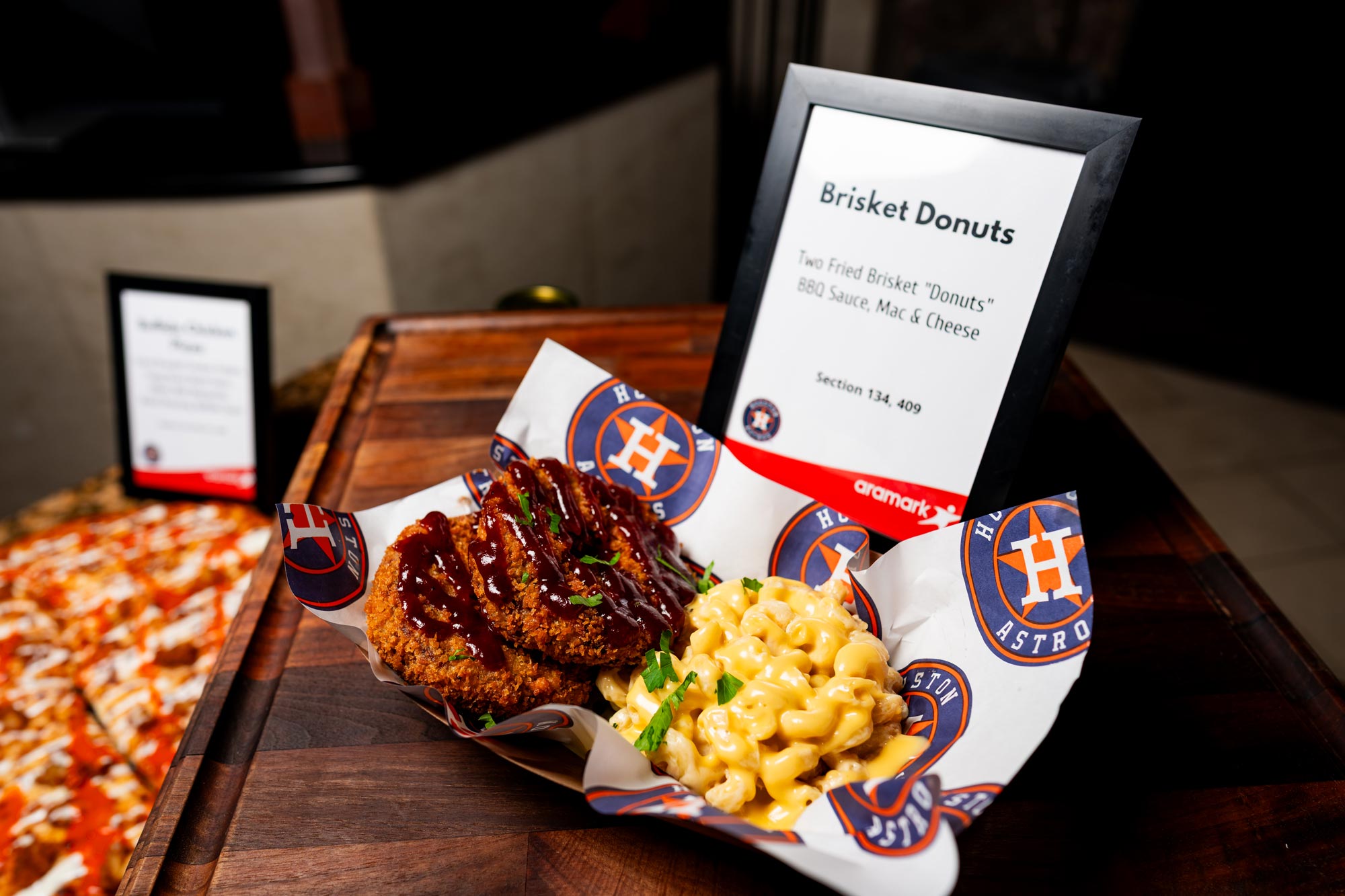 Two brisket donuts covered in barbecue sauce next to a portion of macaroni and cheese inside an Astros food container