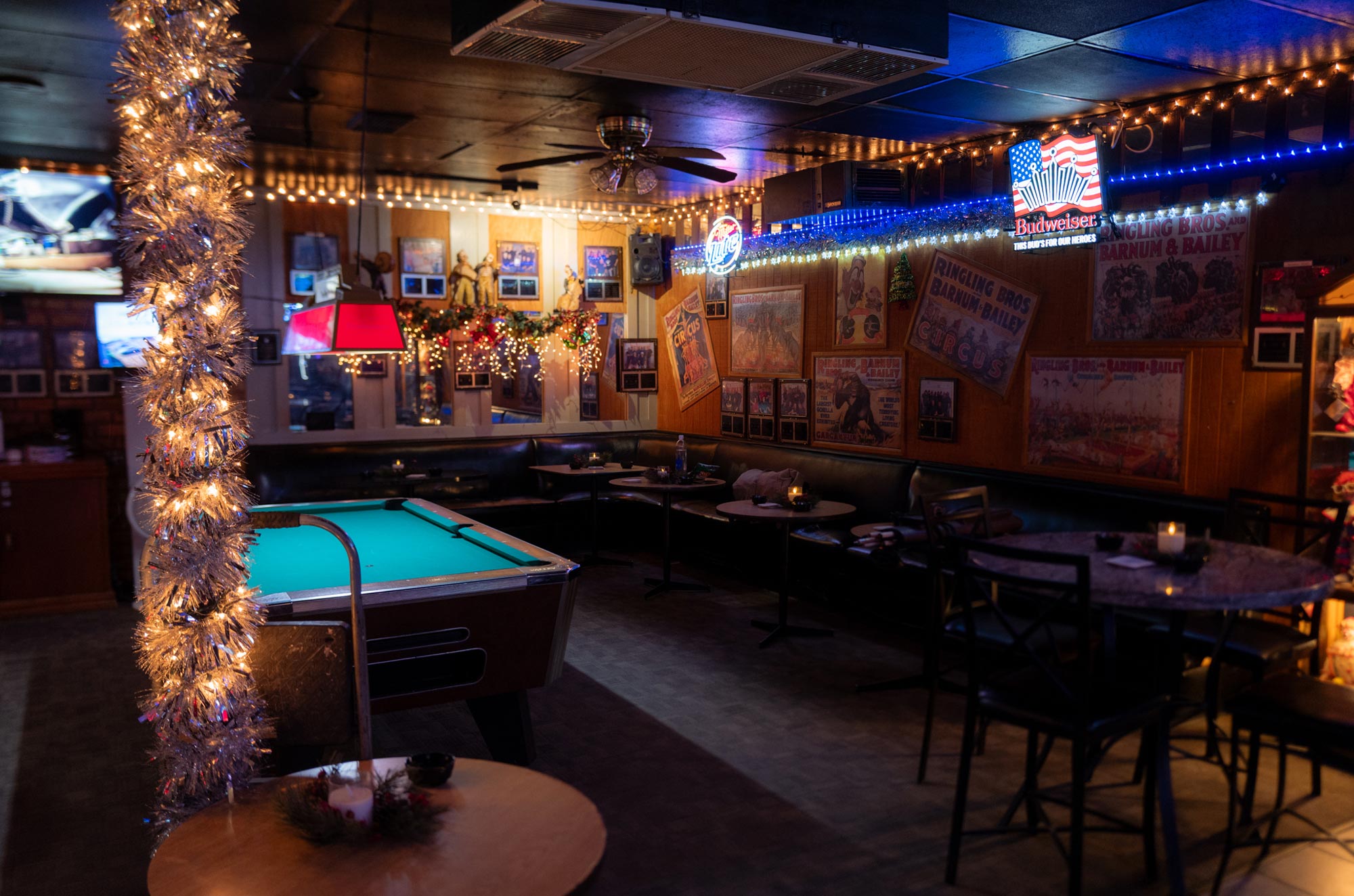 The inside of a bar, lined with black leather booths, the wooden wall covered in Ringling Bros. and other circus posters with a pool table on the left side
