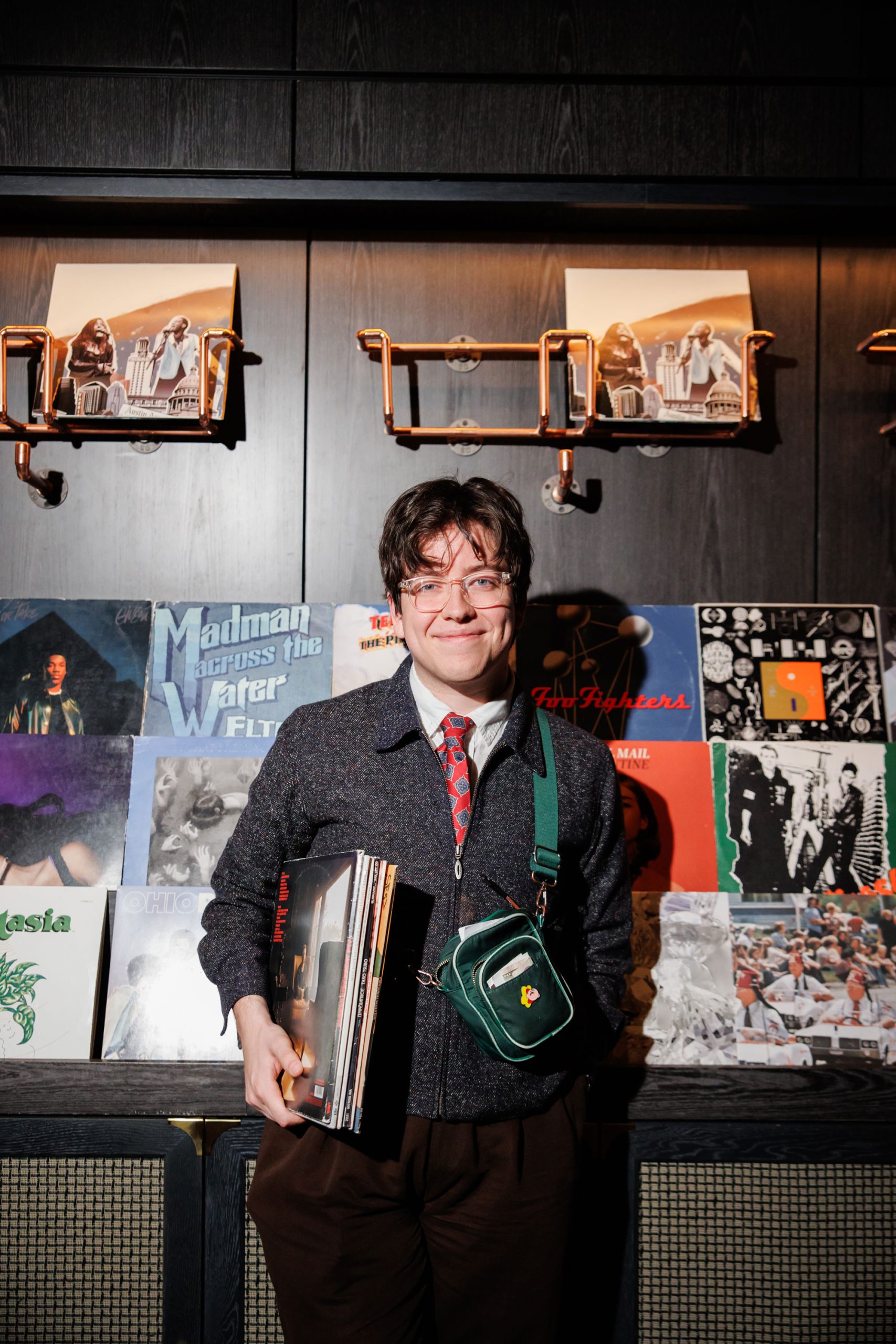 A man in a suit and tie holding vinyl records in front of a display holder with multiple vinyl records