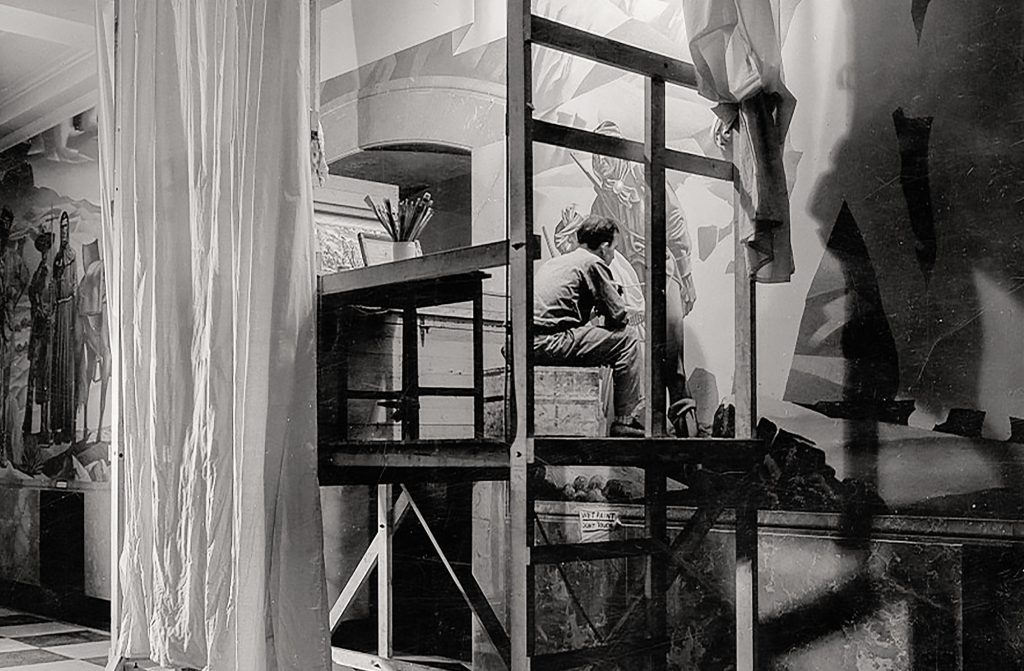 An artist painting while sitting on a wooden platform