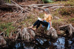 A woman sitting on a riverbank while reading a book