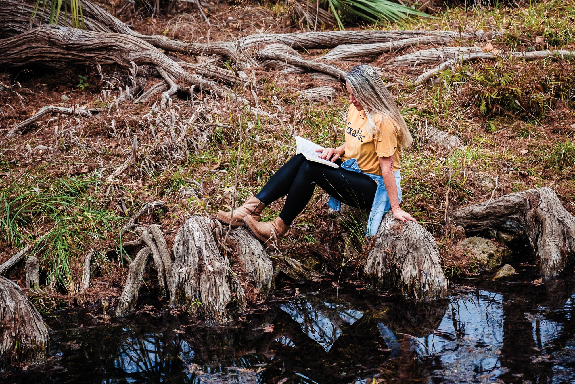 A woman sitting on a riverbank while reading a book