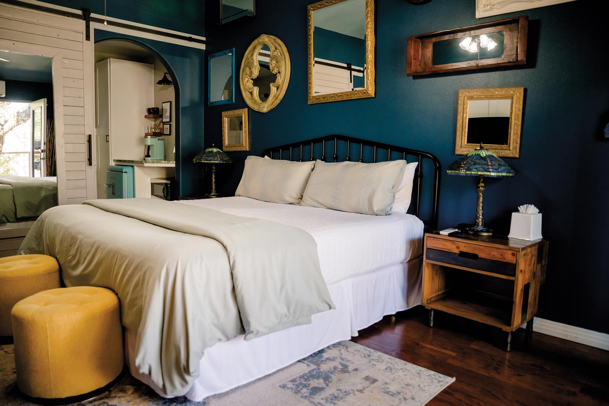 A blue room with multiple mirrors on the wall and a bed with gray linens