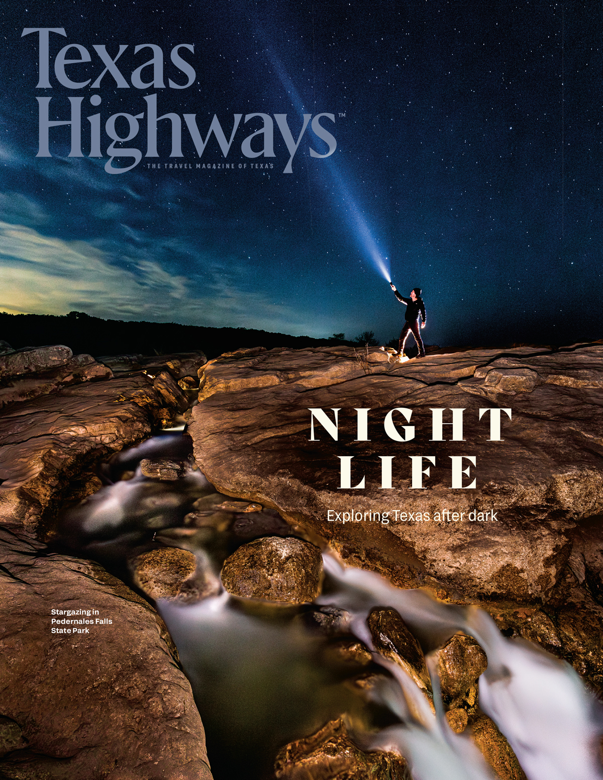 A cover of Texas Highways magazine that reads "Night Life" and shows a person standing on a rocky terrain at night pointing a flashlight into the dark sky