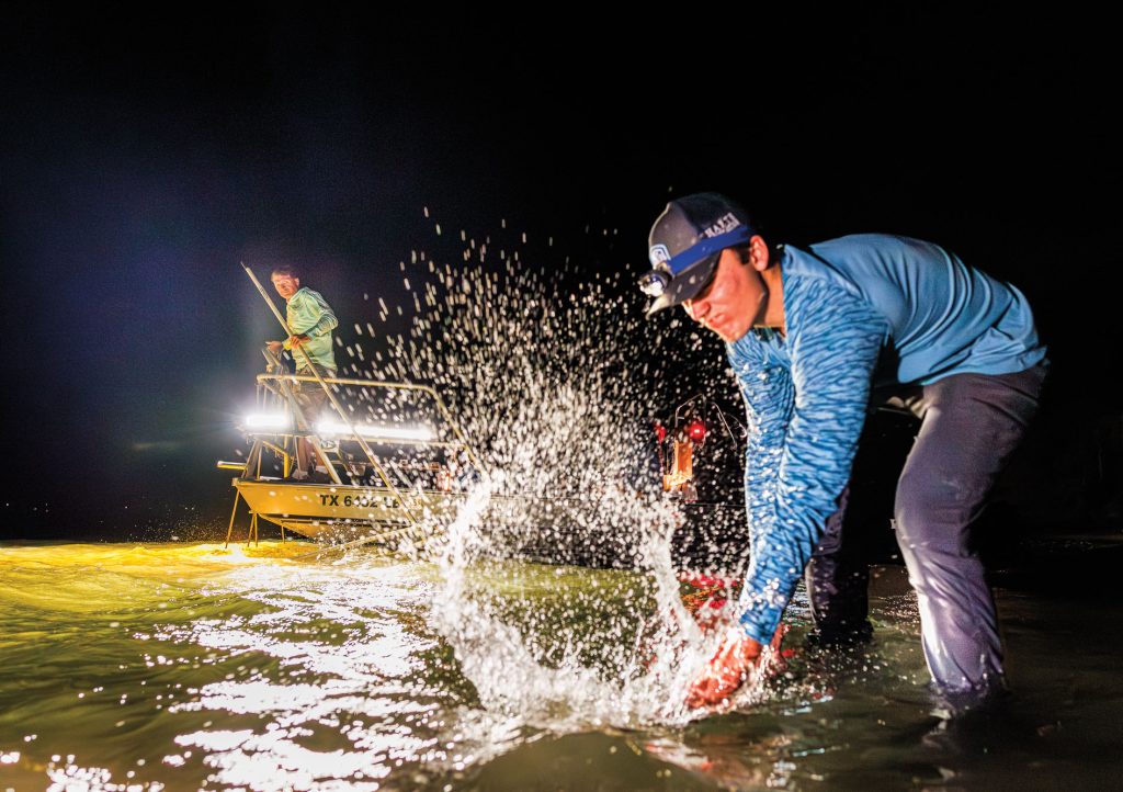 A man creates a splash in illuminated water at night while catching something