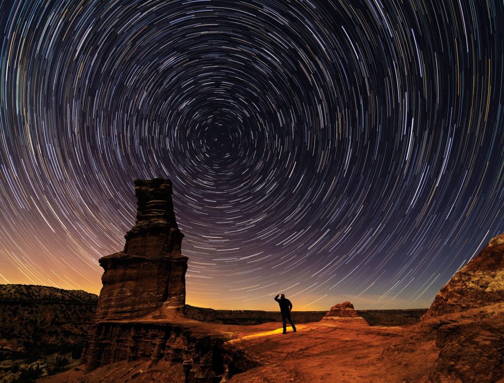 A timelapse of a starry night above a tall rock formation