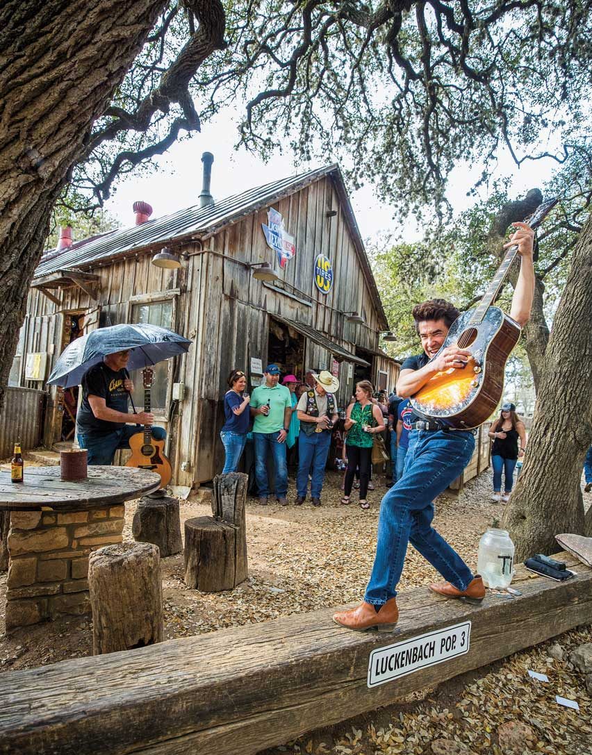 A man on a guitar plays in front of a wooden shack
