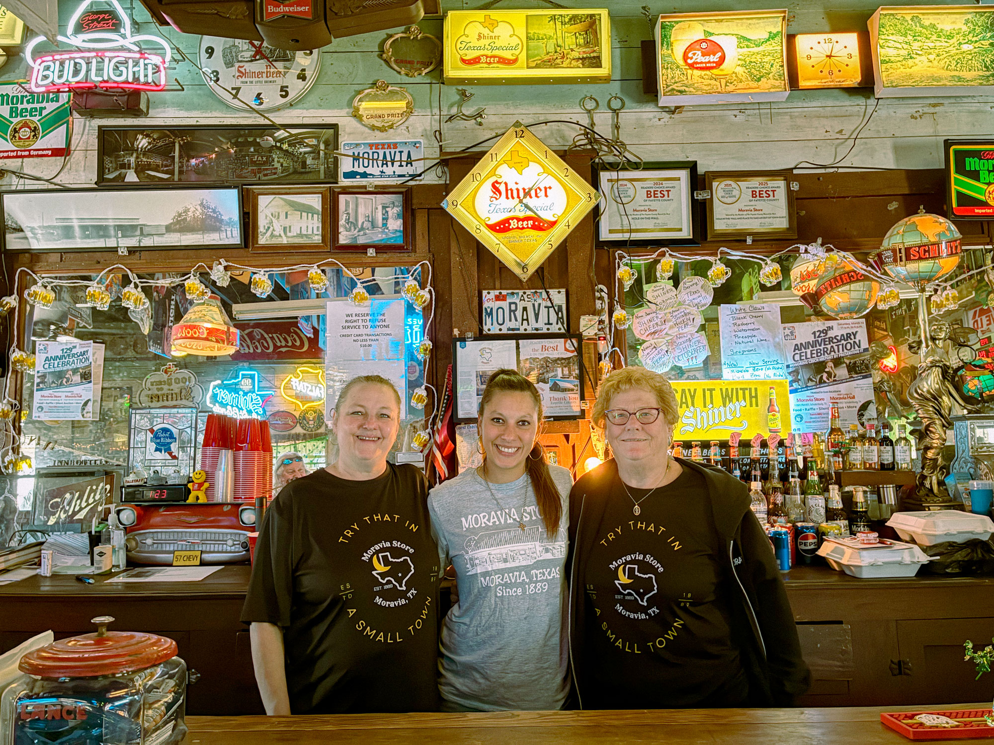 A middle aged woman, a young adult woman, and an older woman pose in front of a bar