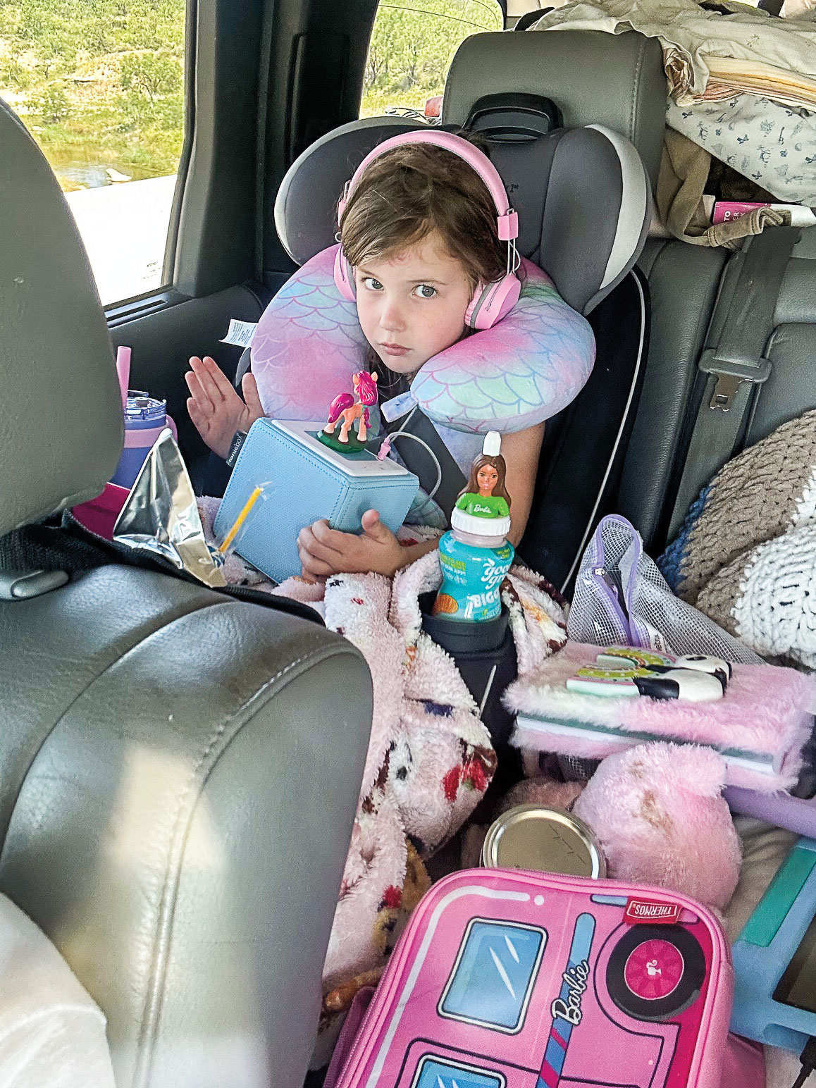 A little girl in a carseat waering headphones, a neck pillow, and blankets