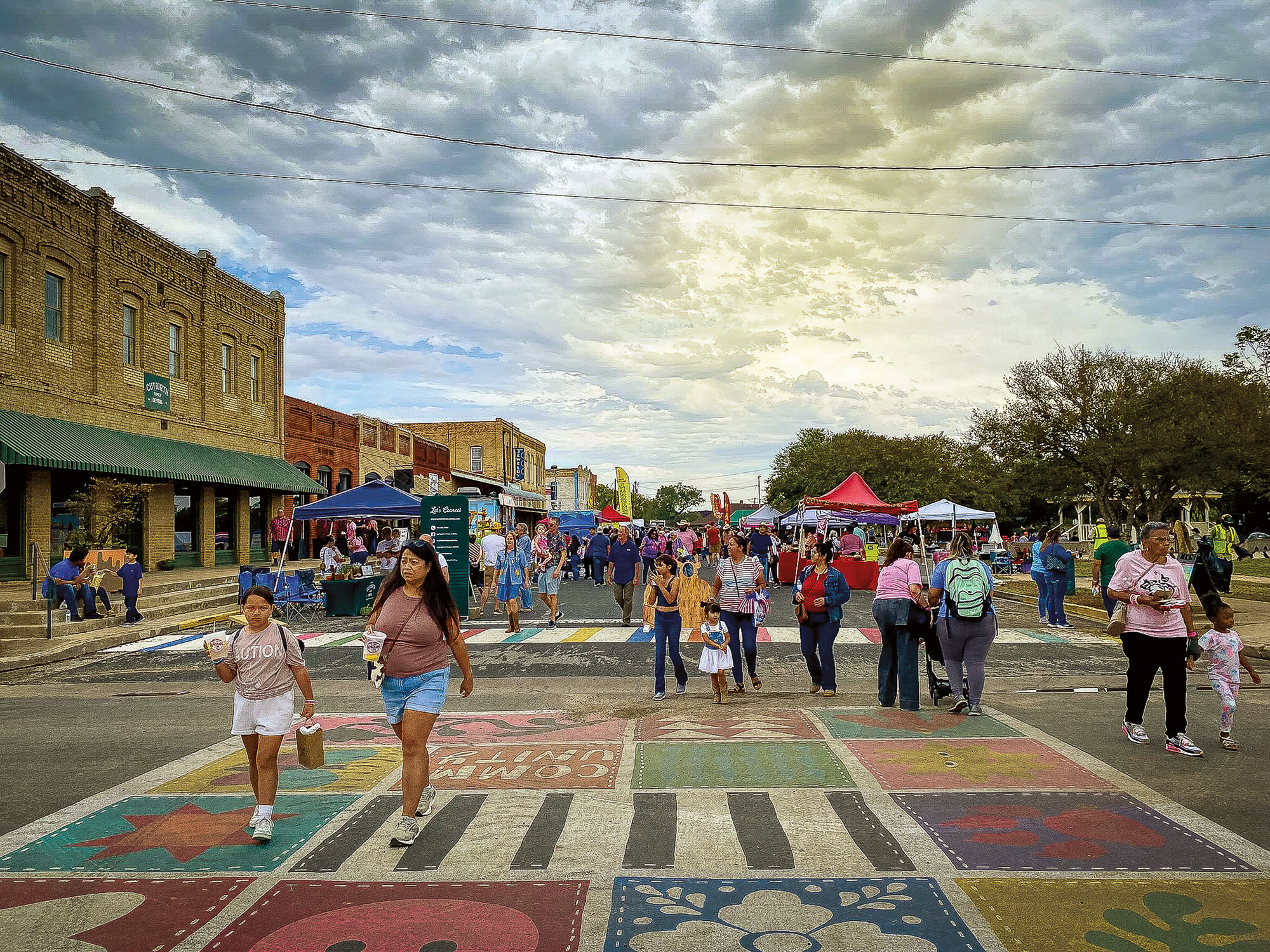 People walking during a street fair near colorful tents atop a colorful, painted sidewalk