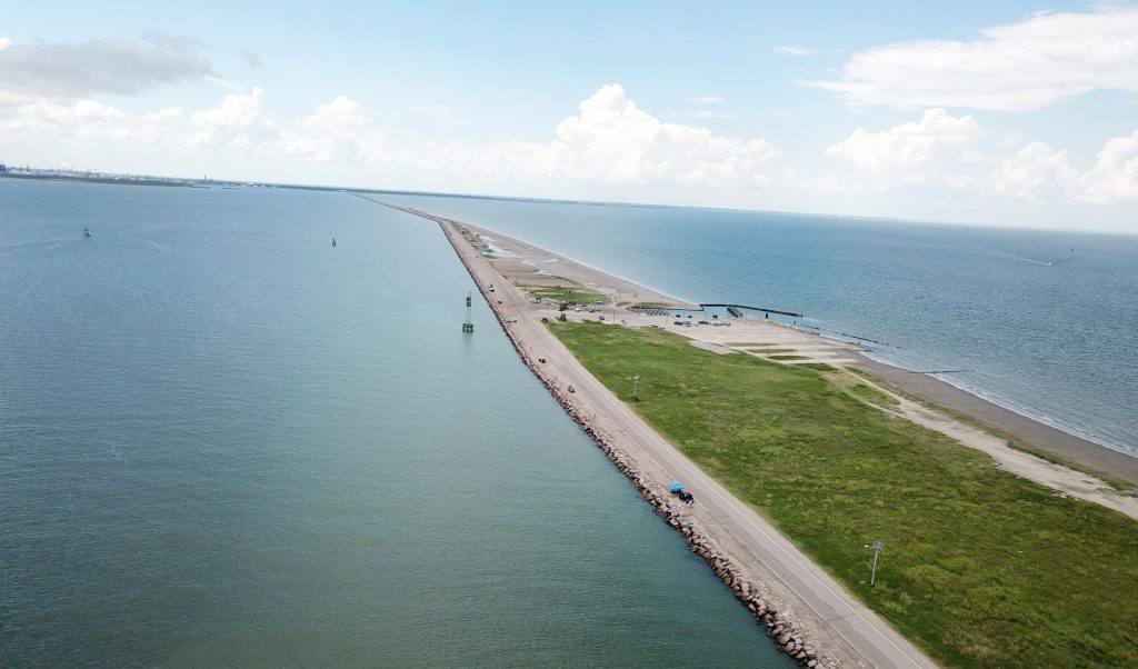 A long road jutting out into the water with cloudy skies above