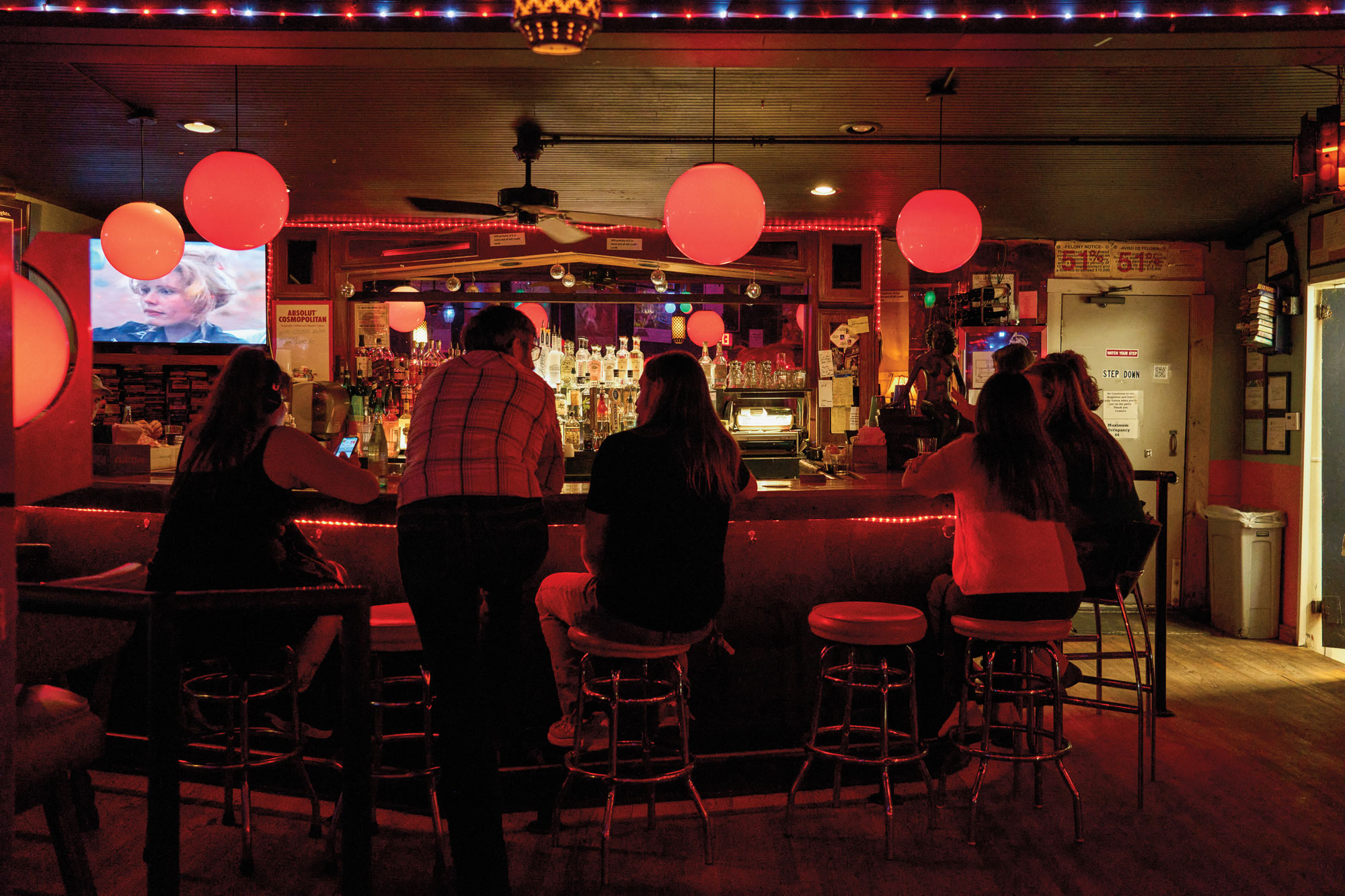 A photograph from behind of people sitting at a darkly lit bar with circular red lights above them