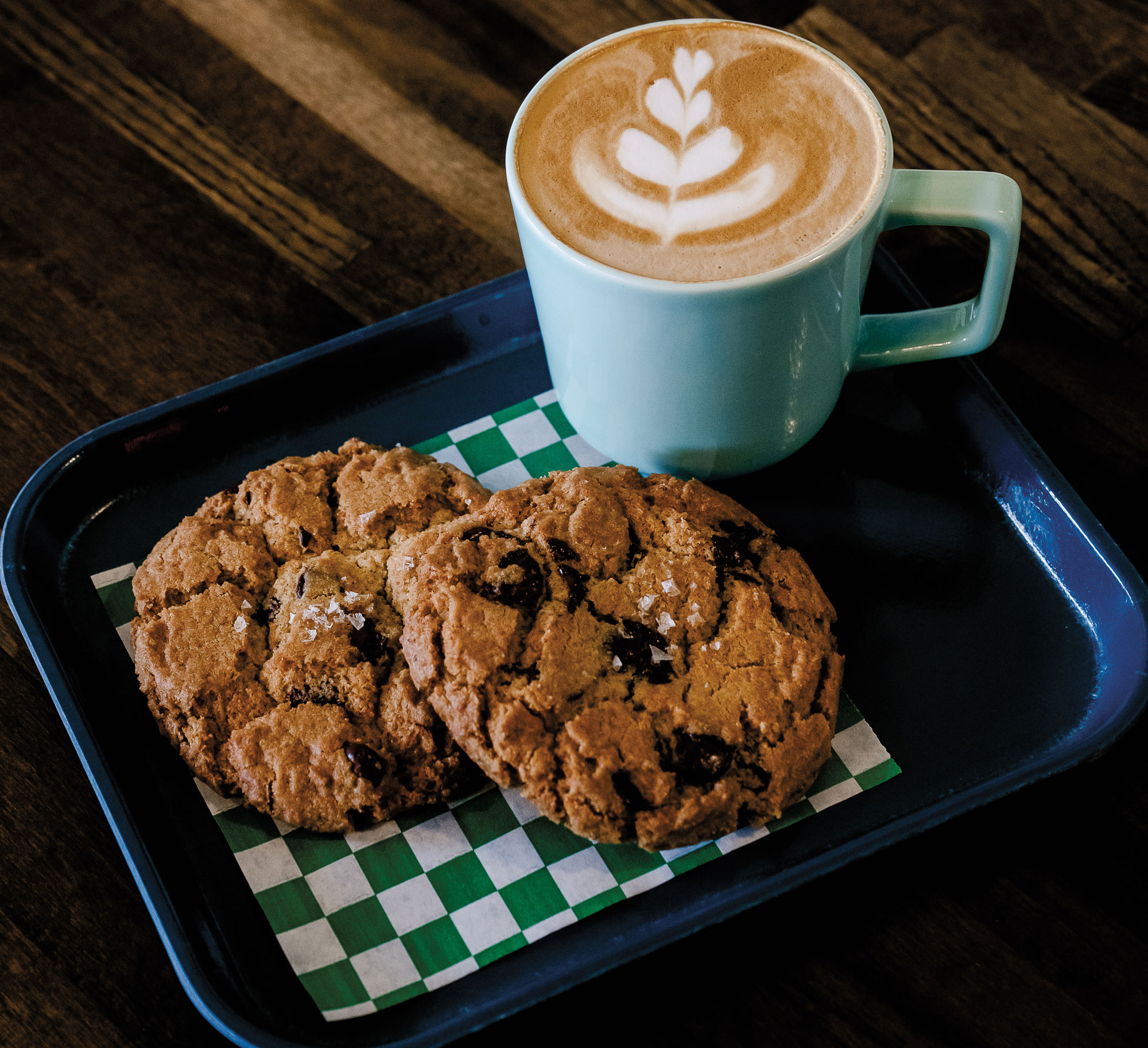 A blue tray with two salted chocolate chip cookies and a coffee drink atop it