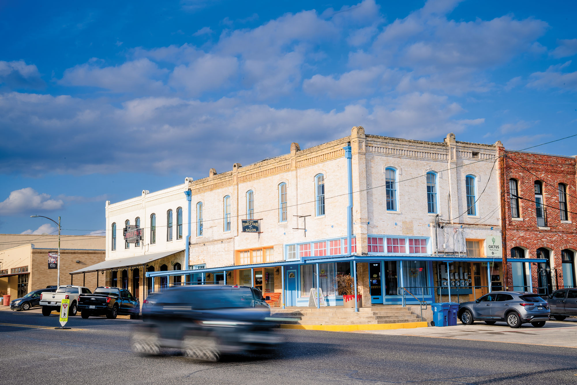 A car driving down a main street in front of older buildings with colorful facades