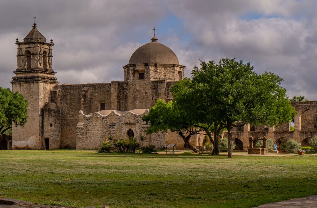 A large stone structure with a turret on the left and a dome on the right with three trees in front