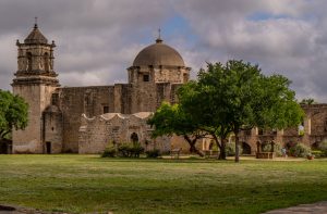 A large stone structure with a turret on the left and a dome on the right with three trees in front
