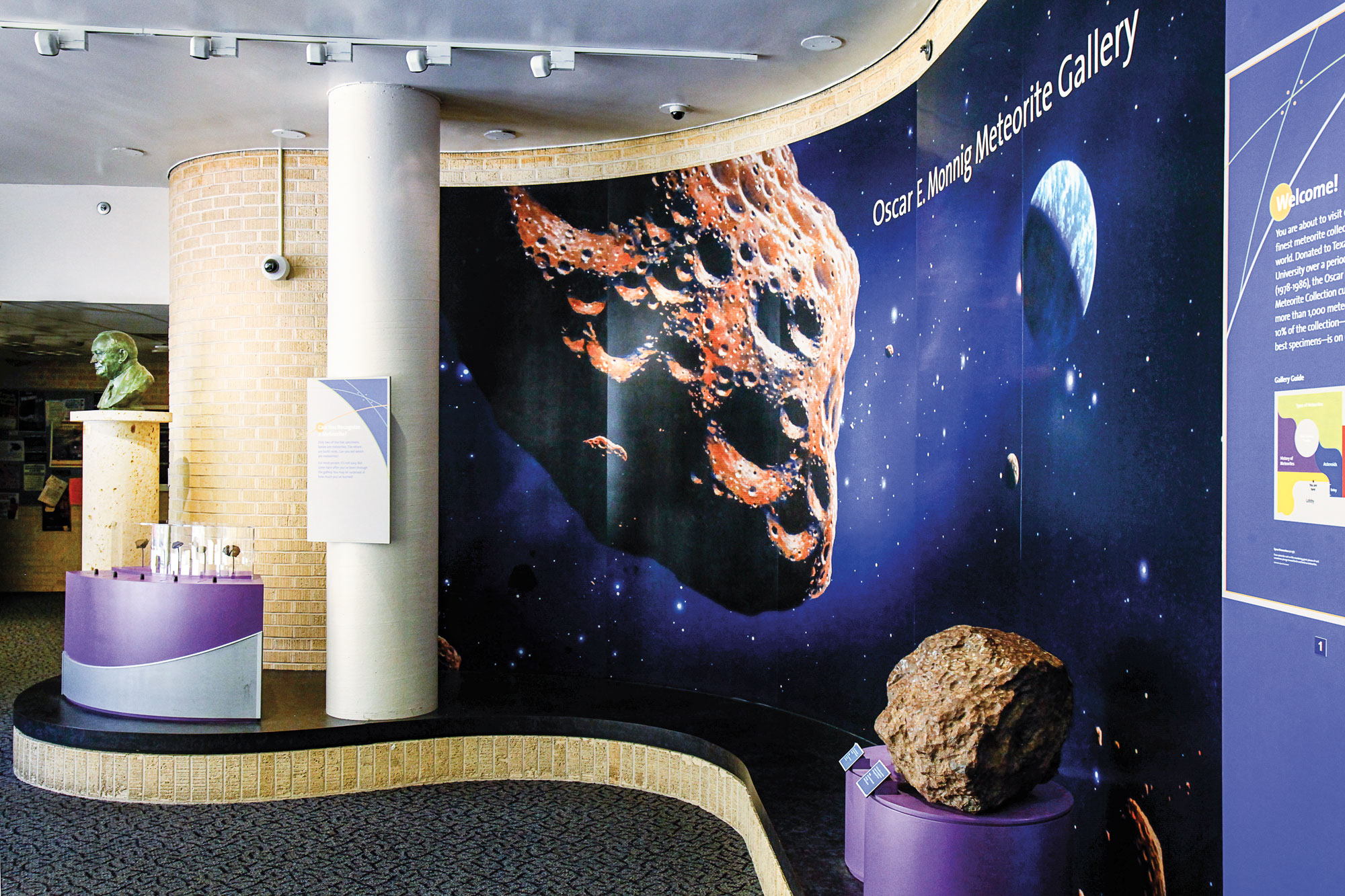 A museum display that reads Oscar E. Monnig Meteorite Gallery with images of a meteorite and outer space behind a display with an actual meteorite on a purple pedestal