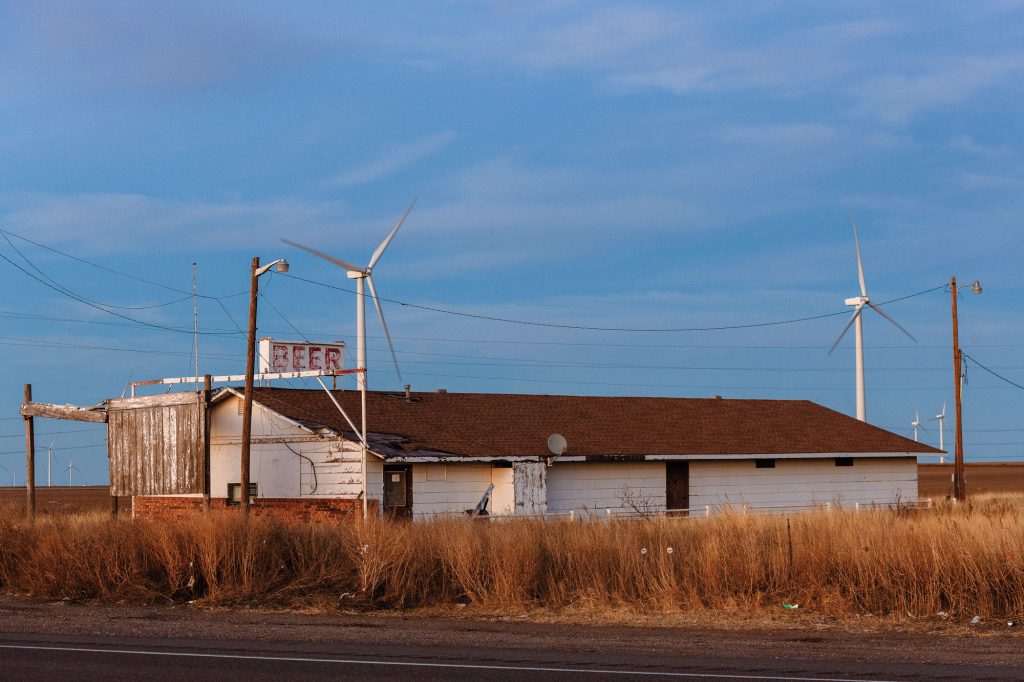 A faded white building with a sign atop it that says BEER in faded red paint between two white windmills