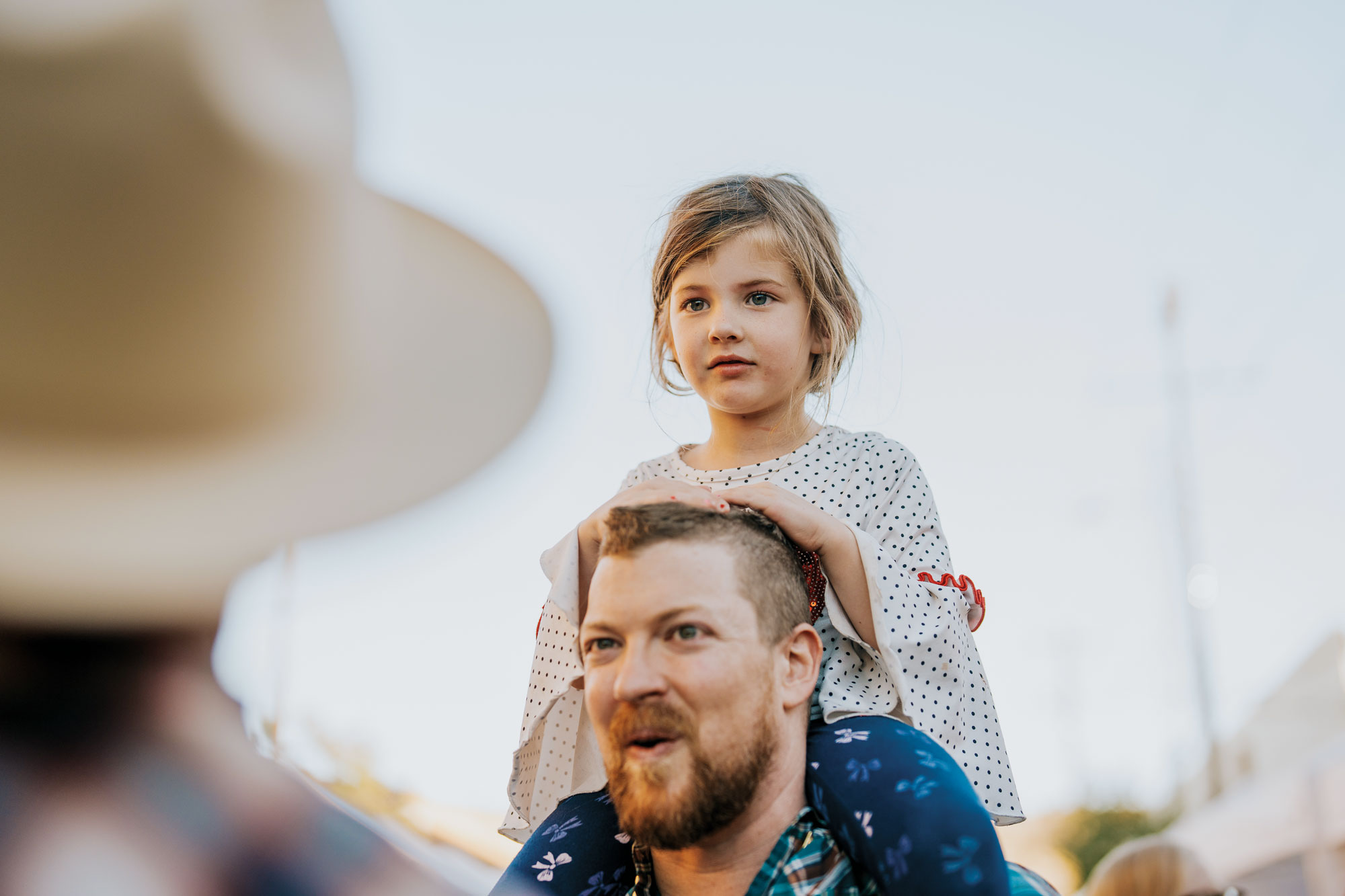 A white man in his late 30s makes an amused expression while carrying a small blonde girl on his shoulders