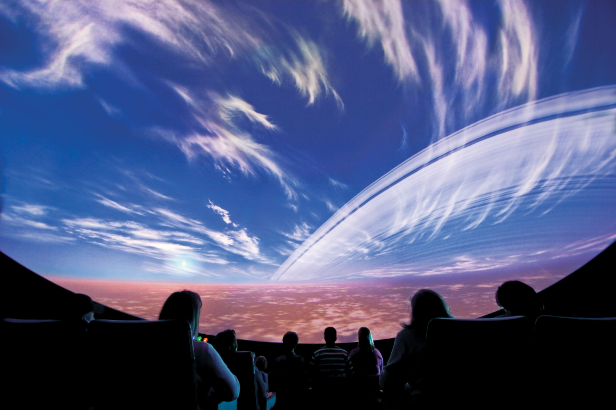 People in a dark auditorium peer into a giant simulation screen of the sky