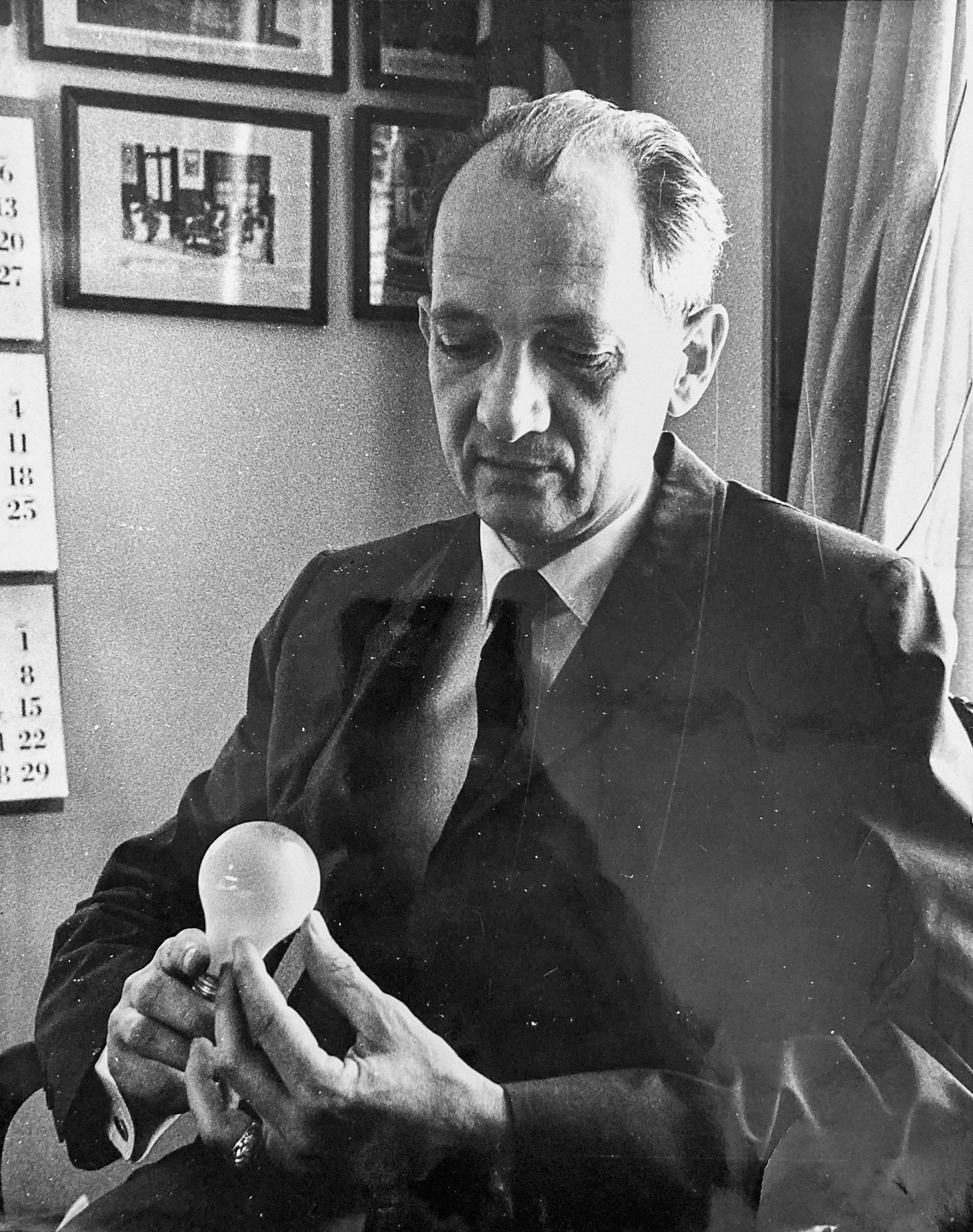 A black and white photo of a man in a suit holding a light bulb pensively
