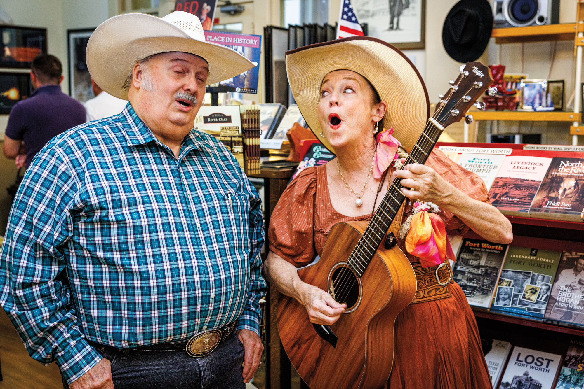 A man and woman dressed in cowboy hats sing while the woman plays a guitar