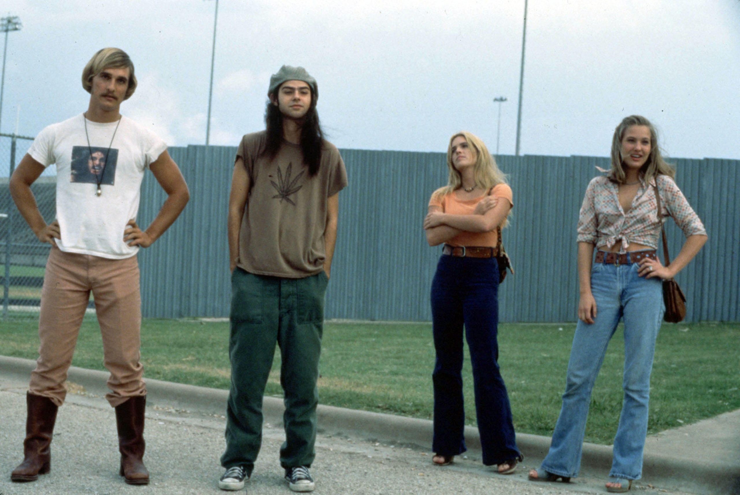 Two men and two women dressed in 1970s attire stand defiantly in front of a football field