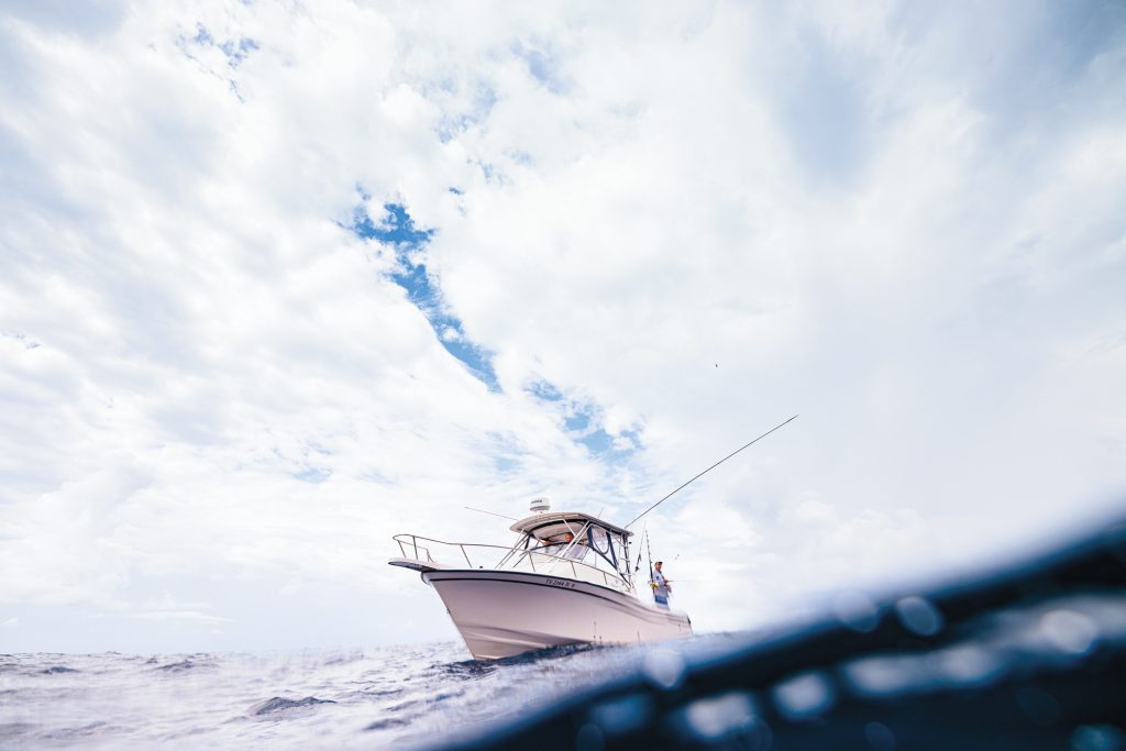 A white fishing boat with three people abord under a cloudy sky