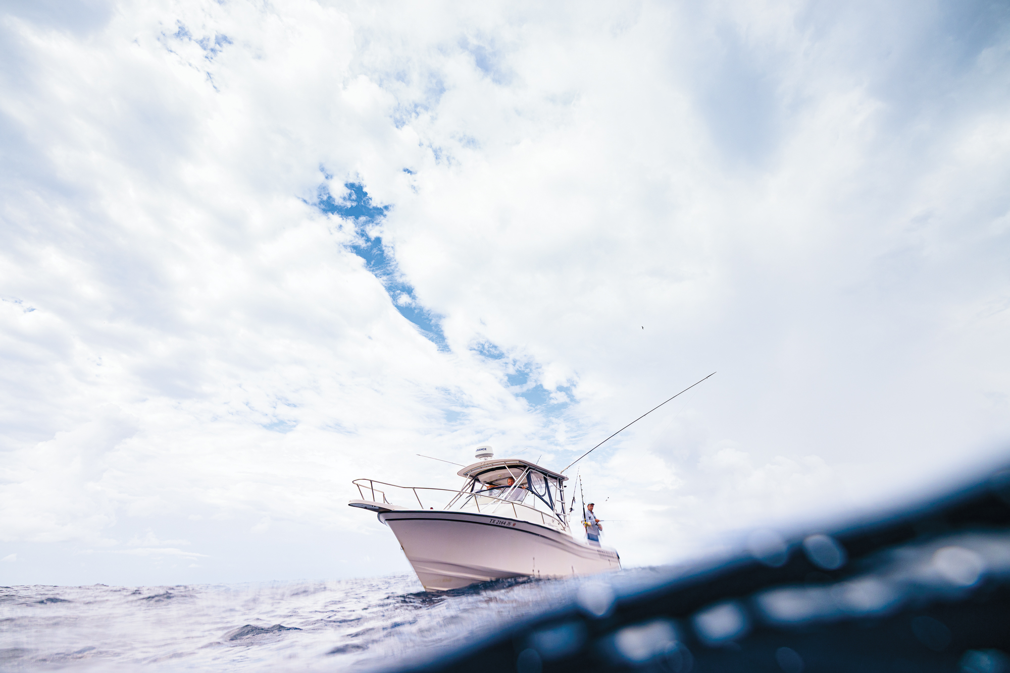 A white fishing boat with three people abord under a cloudy sky