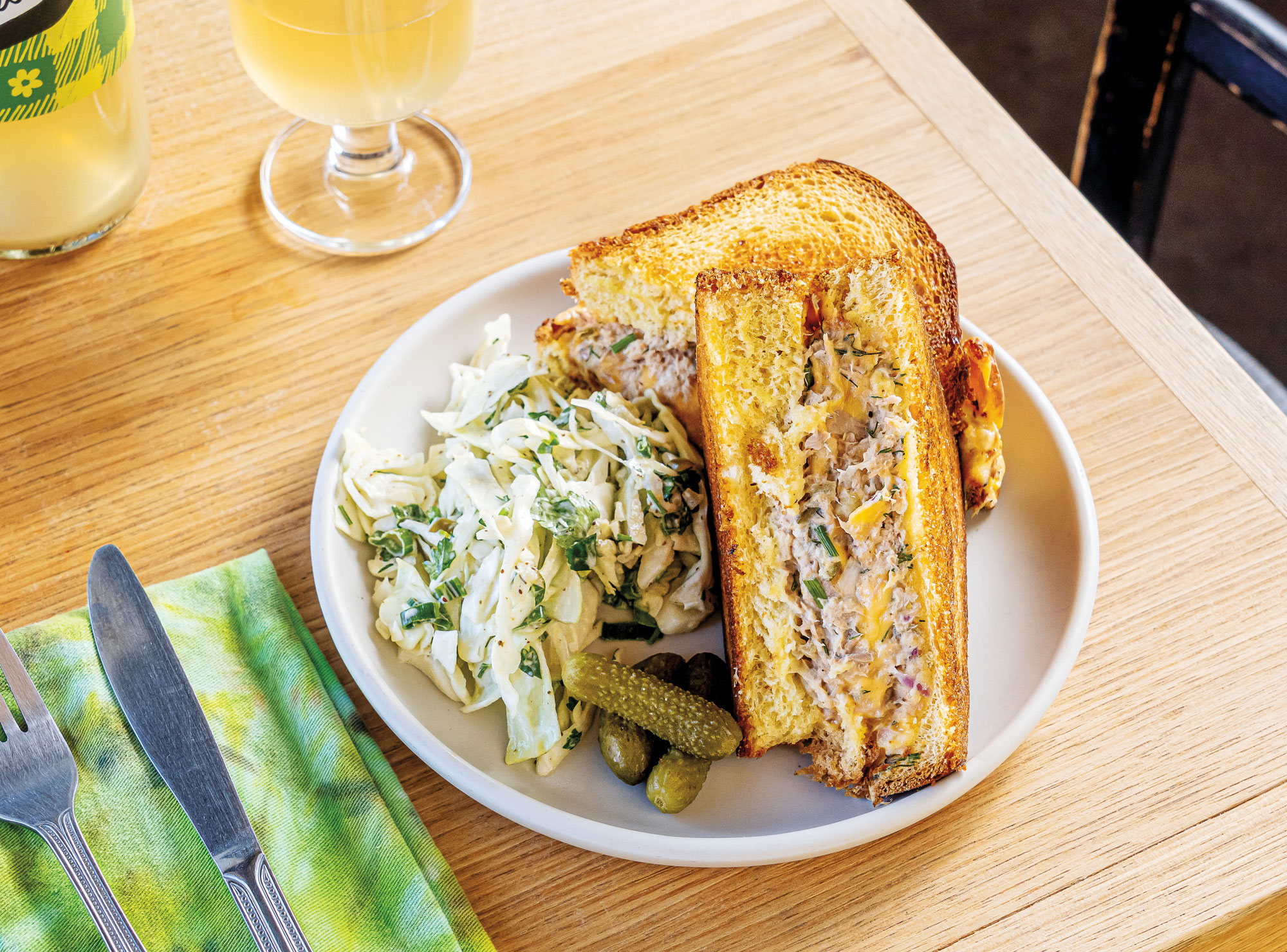 A tuna melt sandwich on a white plate next to cole slaw atop a wooden table