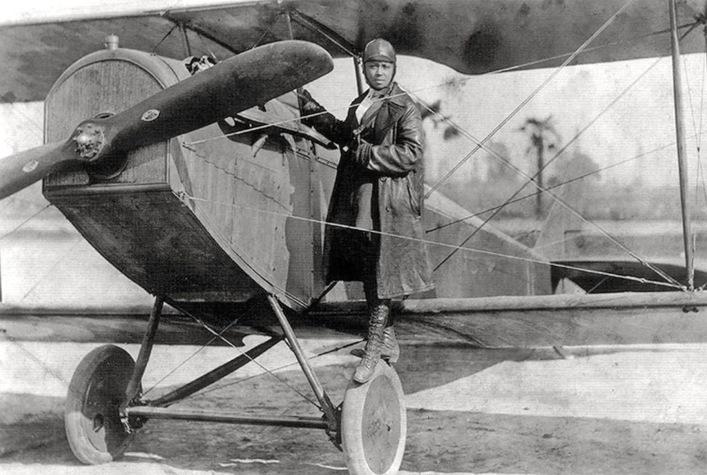 A woman pilot standing on the wheel of an old airplane