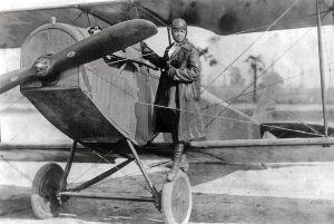 A woman pilot standing on the wheel of an old airplane